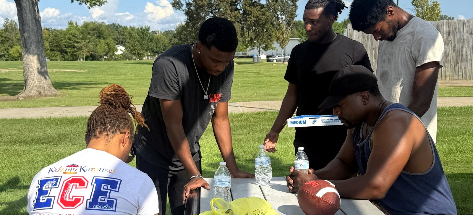 RaqGiveback team members gathered around a picnic table with pizza and water.
